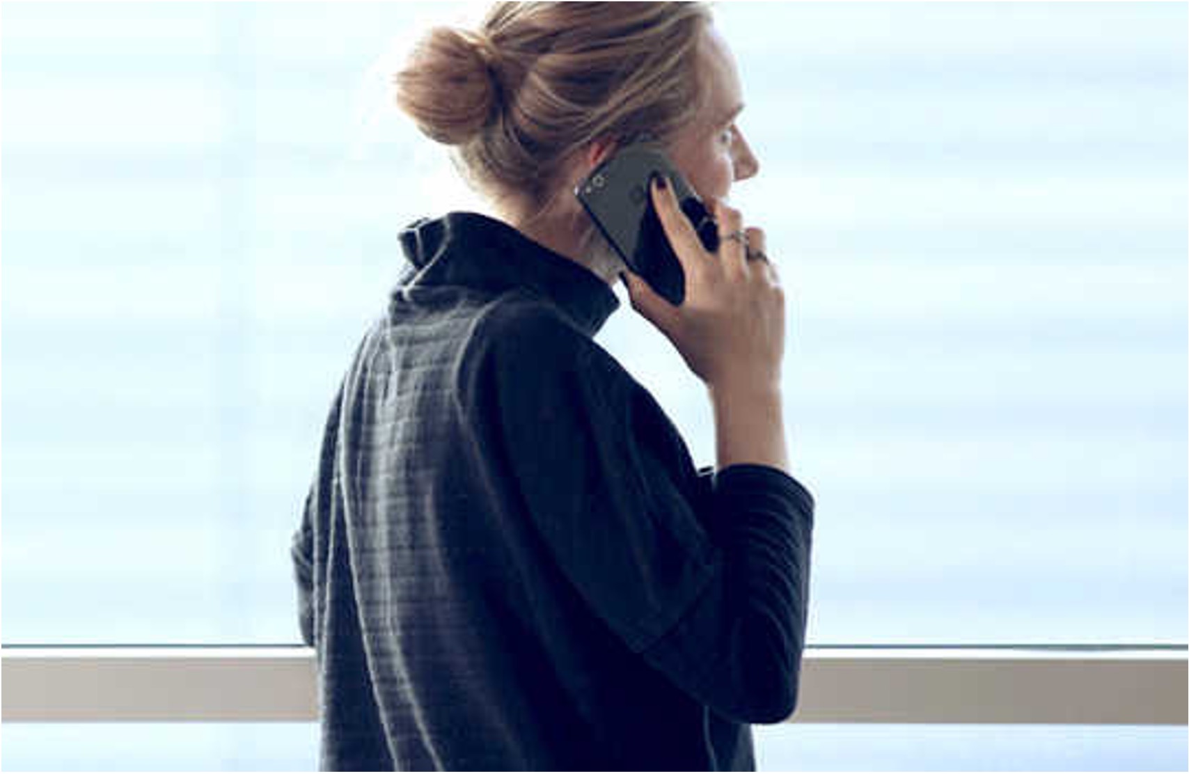 Nummerportering til erhverv Kvinde taler i mobiltelefon om nummerportering til erhverv ved et vindue med udsigt til en lys baggrund